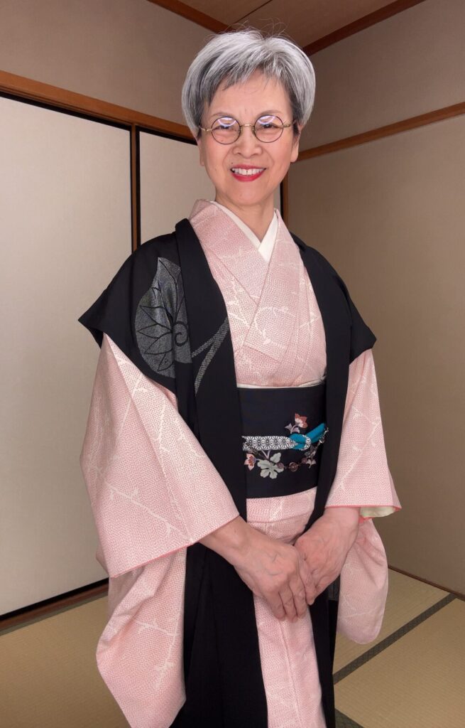 派手な紬を袖無し羽織で抑えて